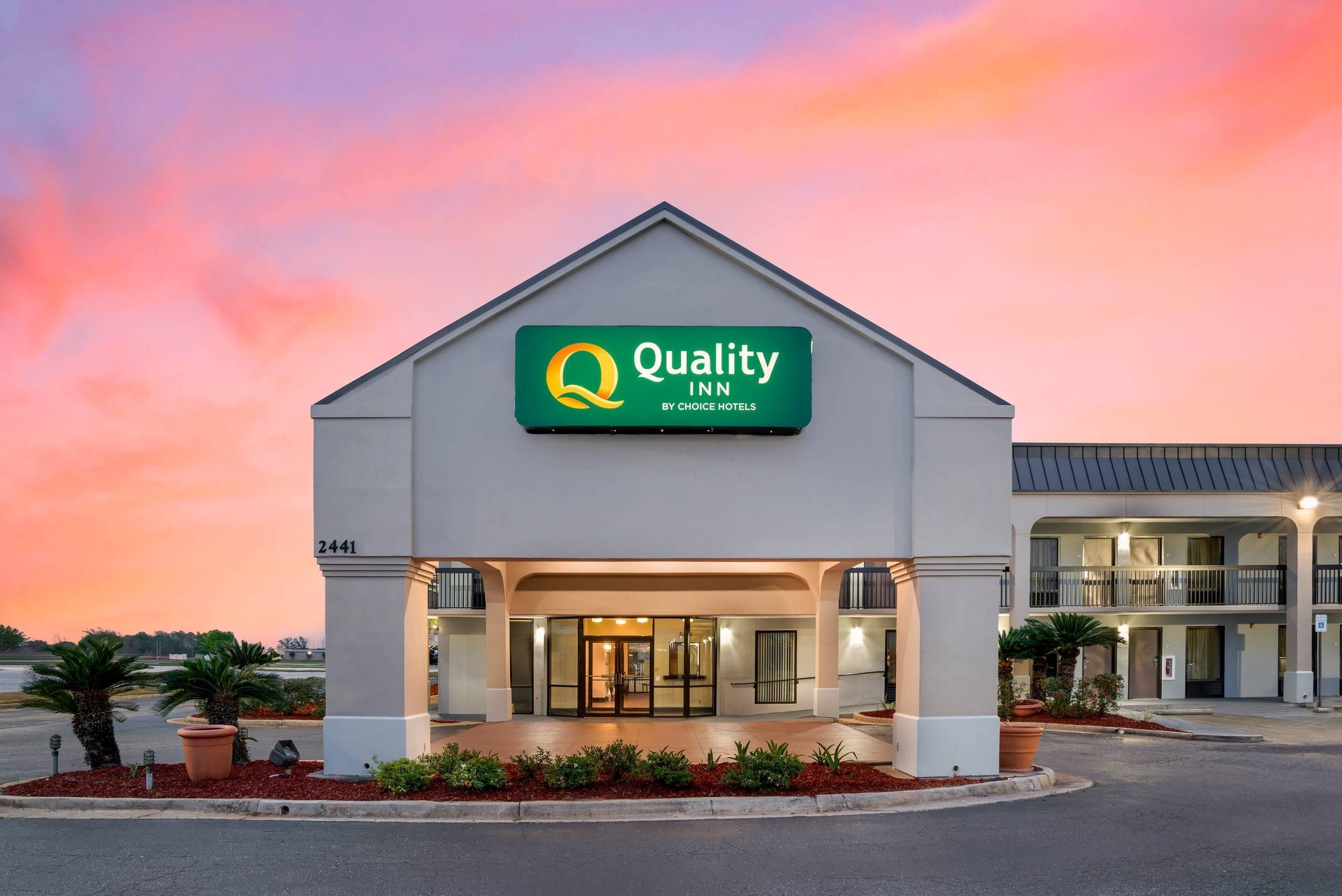 A Quality Inn by Choice Hotels building with a green sign, a covered entrance, and a parking lot with landscaping.