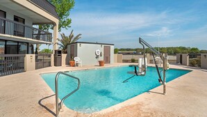 A swimming pool with a metal ladder, a covered seating area, and a small building with a door and windows.