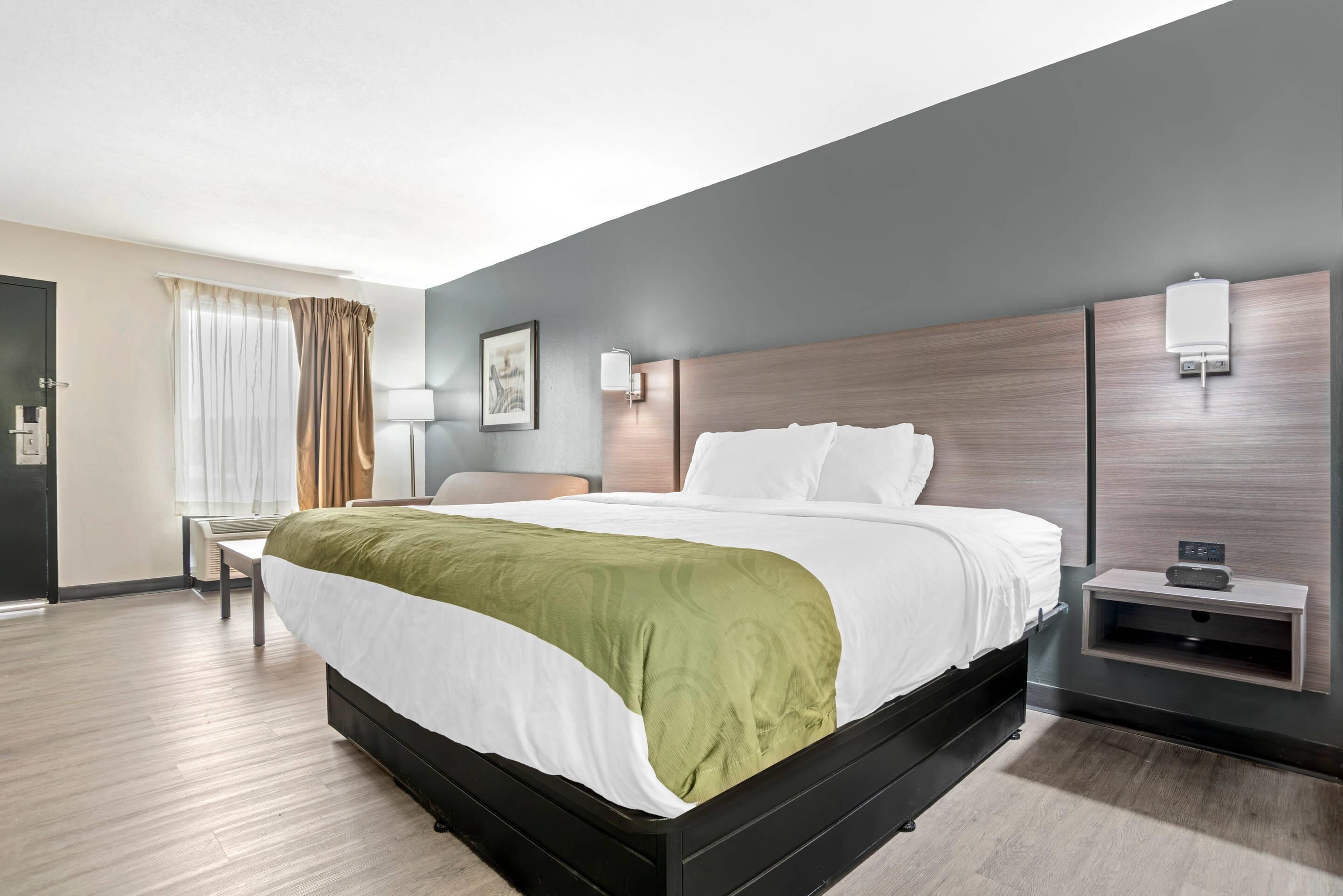 A modern hotel room with a large bed, a bedside table with a lamp, and a wall-mounted TV.