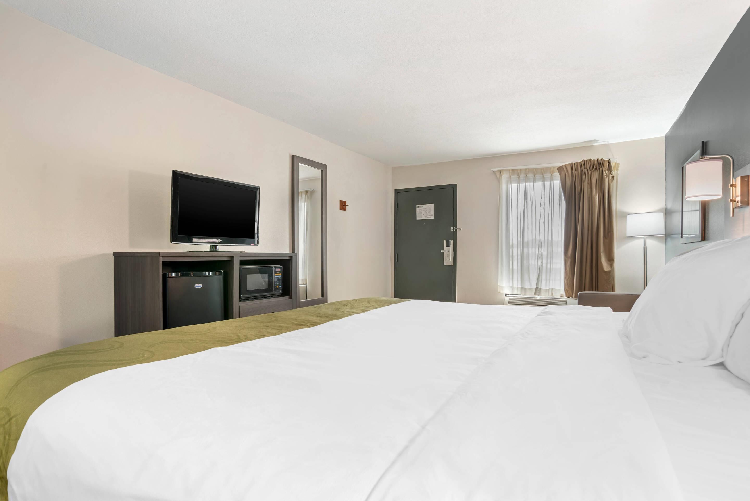 Habitació d'hotel amb llit, televisió, microones, escriptori i finestra amb cortines.