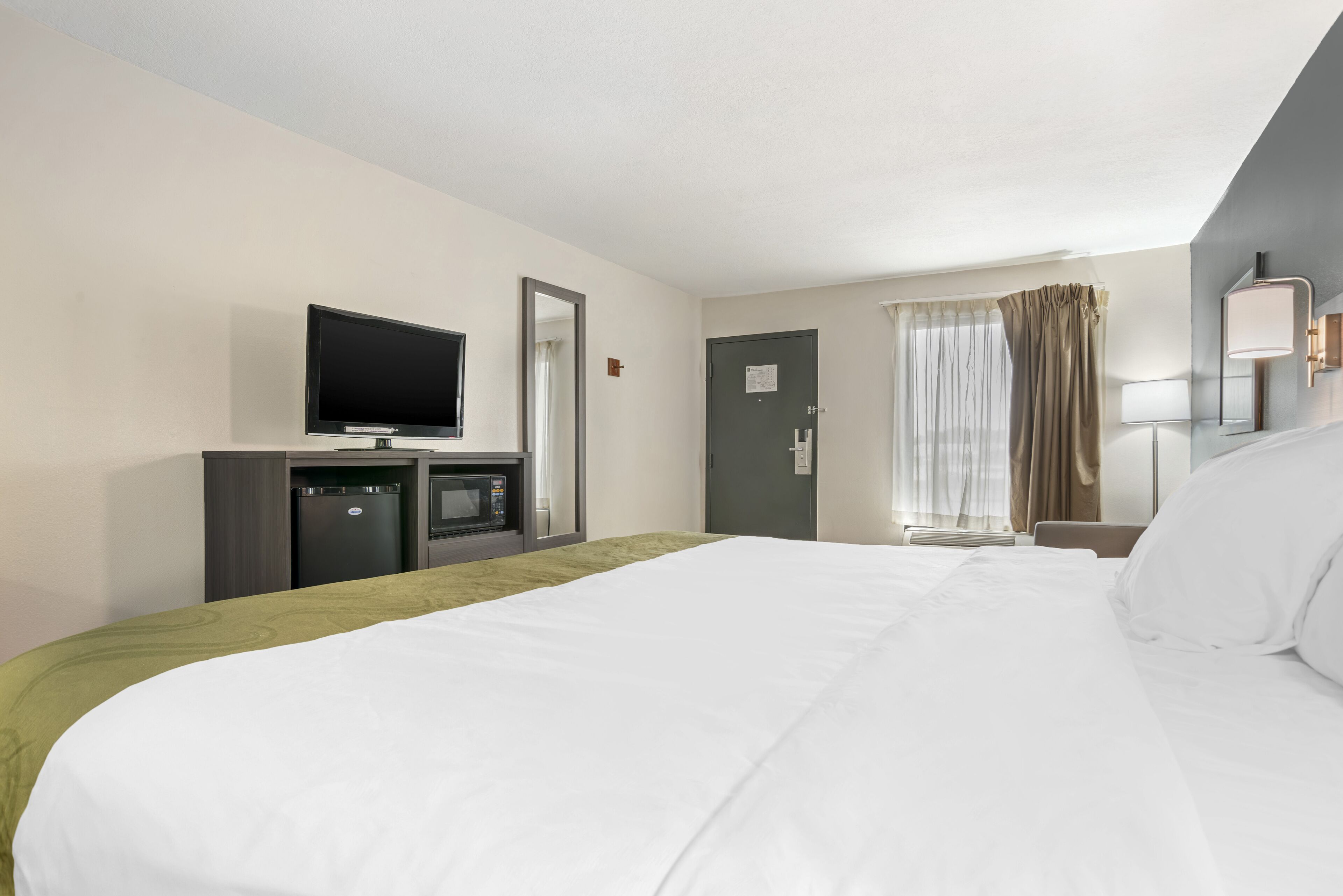 Een hotelkamer met een bed, een televisie, een magnetron, een deur en een raam met gordijnen.