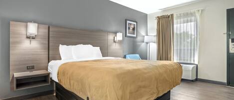 A modern hotel room with a large bed, bedside tables, a lamp, and a window with curtains.