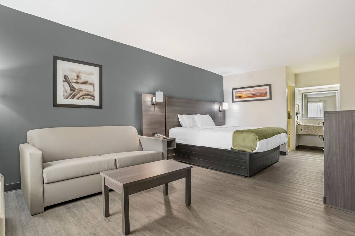 Una camera d'albergo moderna con una parete grigia, un letto con biancheria bianca, un divano grigio, un comodino in legno e un tavolino.