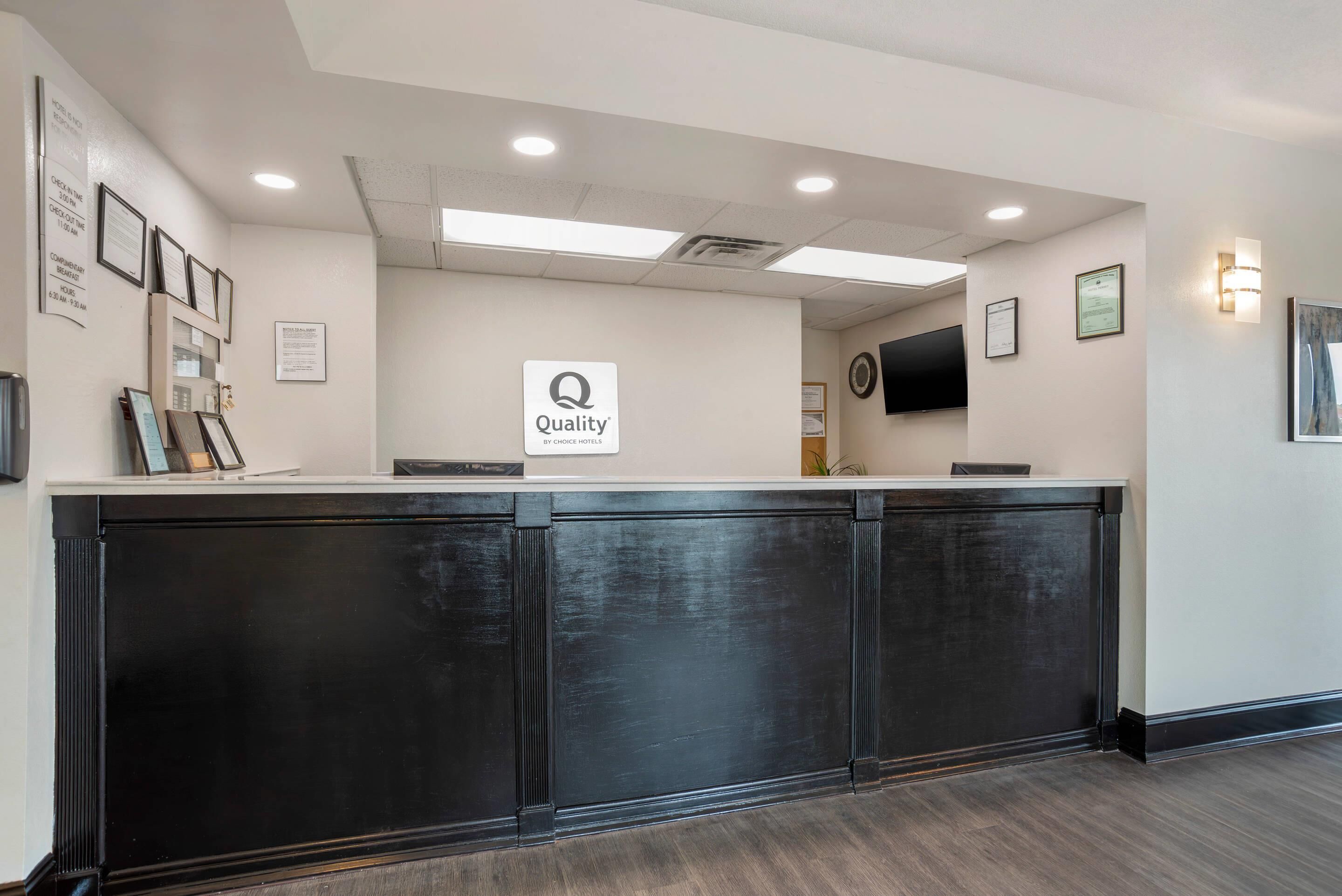 Un comptoir d’accueil avec une enseigne indiquant « Qualité garantie par Choice Hotels », des certificats encadrés accrochés au mur et un téléviseur à écran plat placé au-dessus du comptoir.