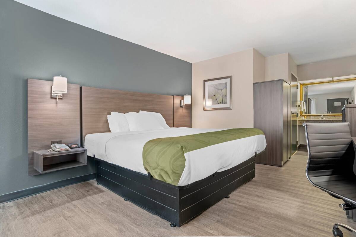 Una camera d'albergo con un letto, un comodino, una lampada e una sedia.