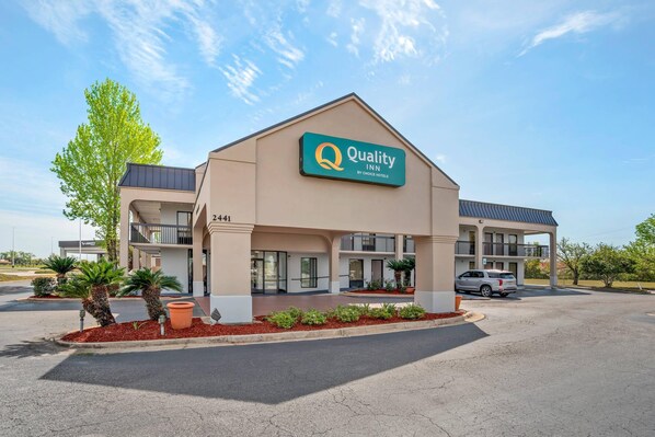 A Quality Inn by Choice Hotels building with a beige facade, a green sign, and a parking lot with a few cars.