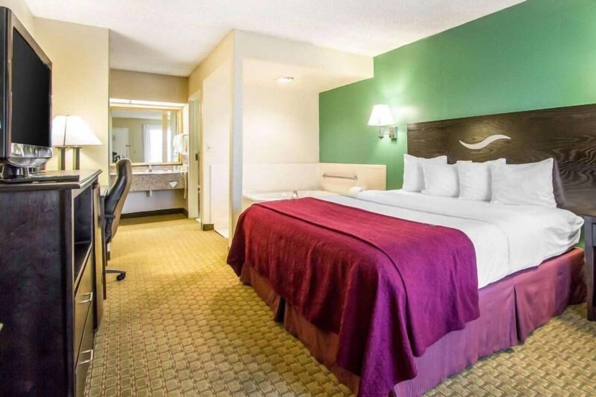 Una camera d'albergo con un letto, una scrivania, una sedia, uno specchio e un televisore.