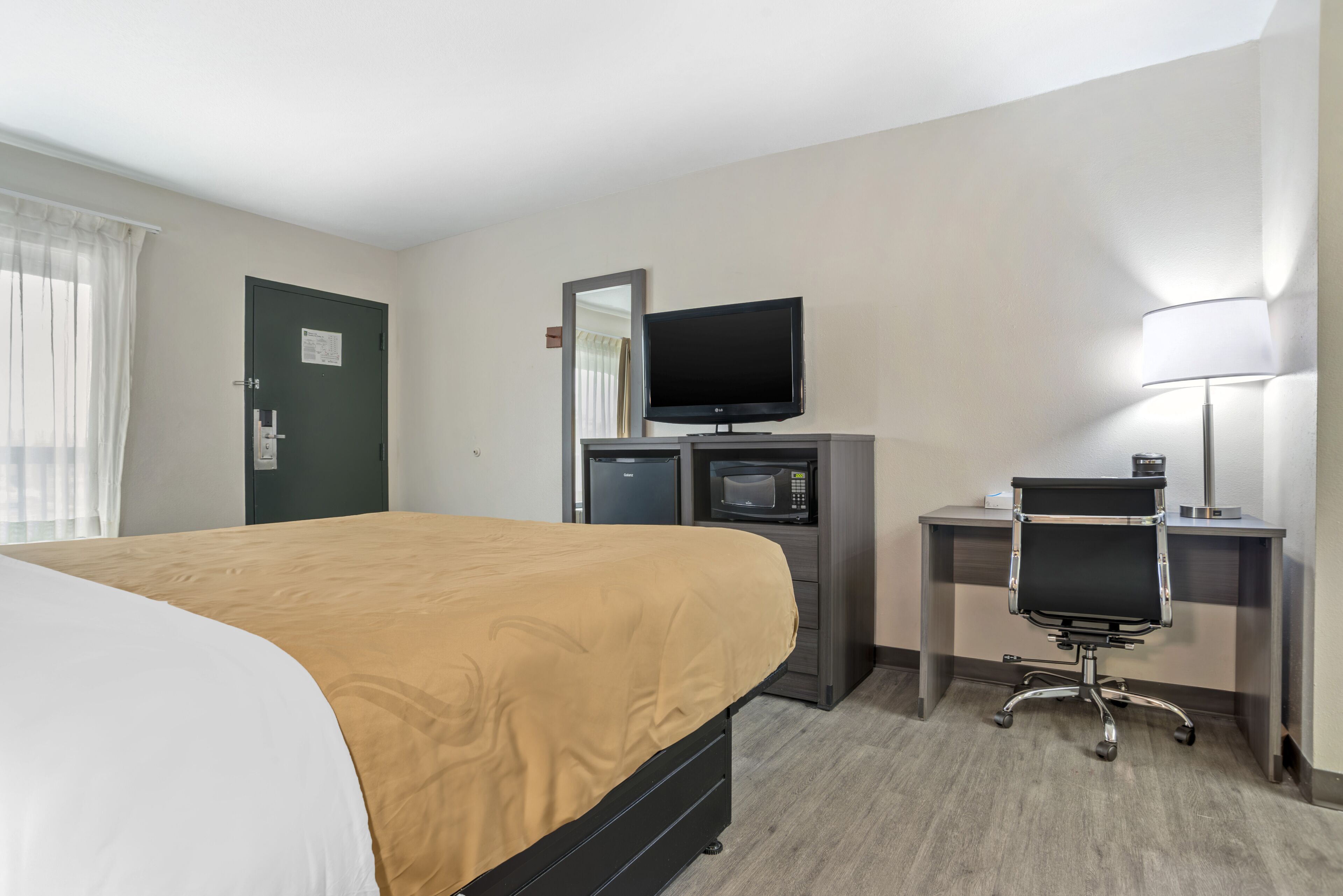 A hotel room with a bed, a desk with a computer, a TV, and a microwave.