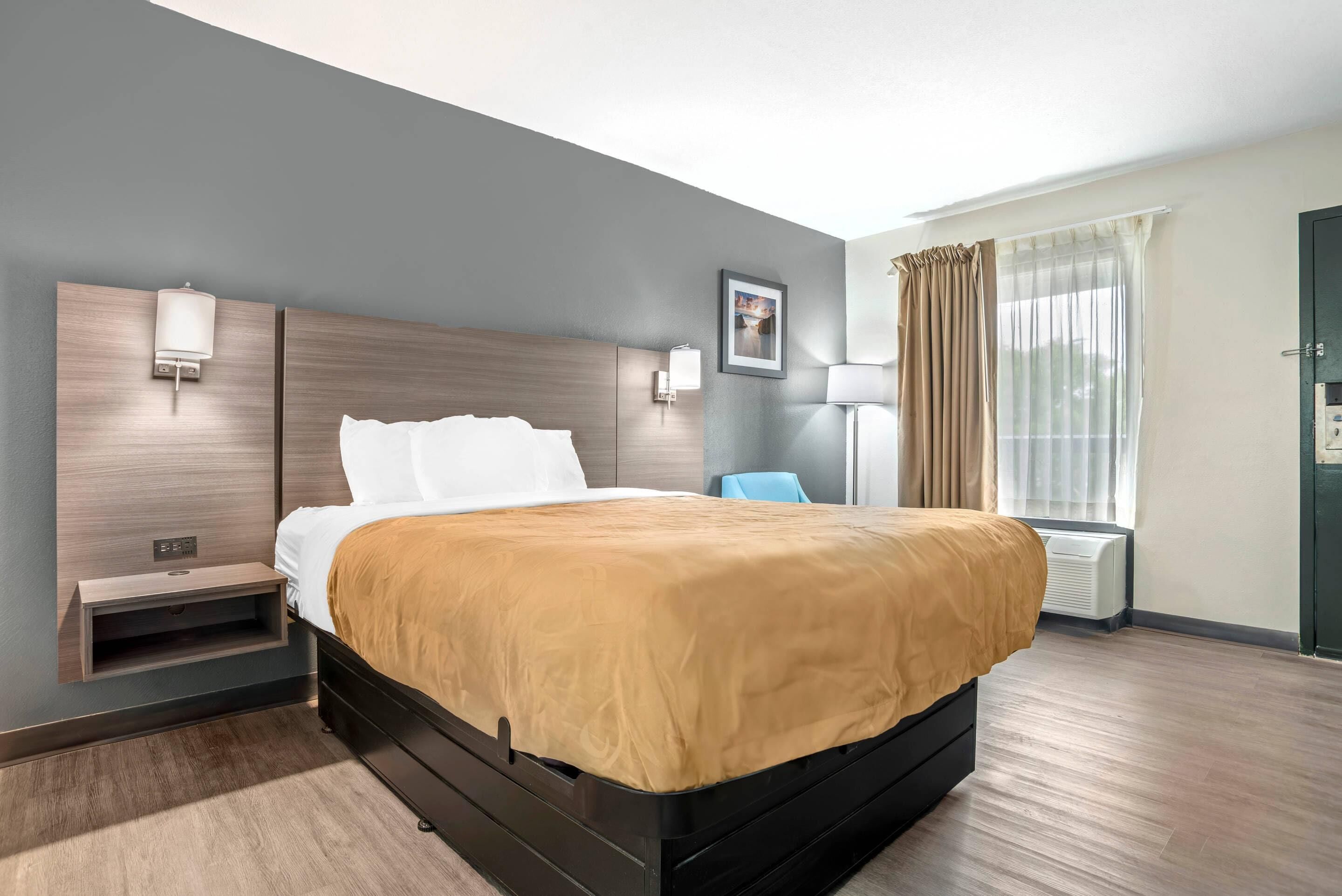 Una habitación de hotel moderna con una cama grande, mesitas de noche, un escritorio y una ventana con cortinas.