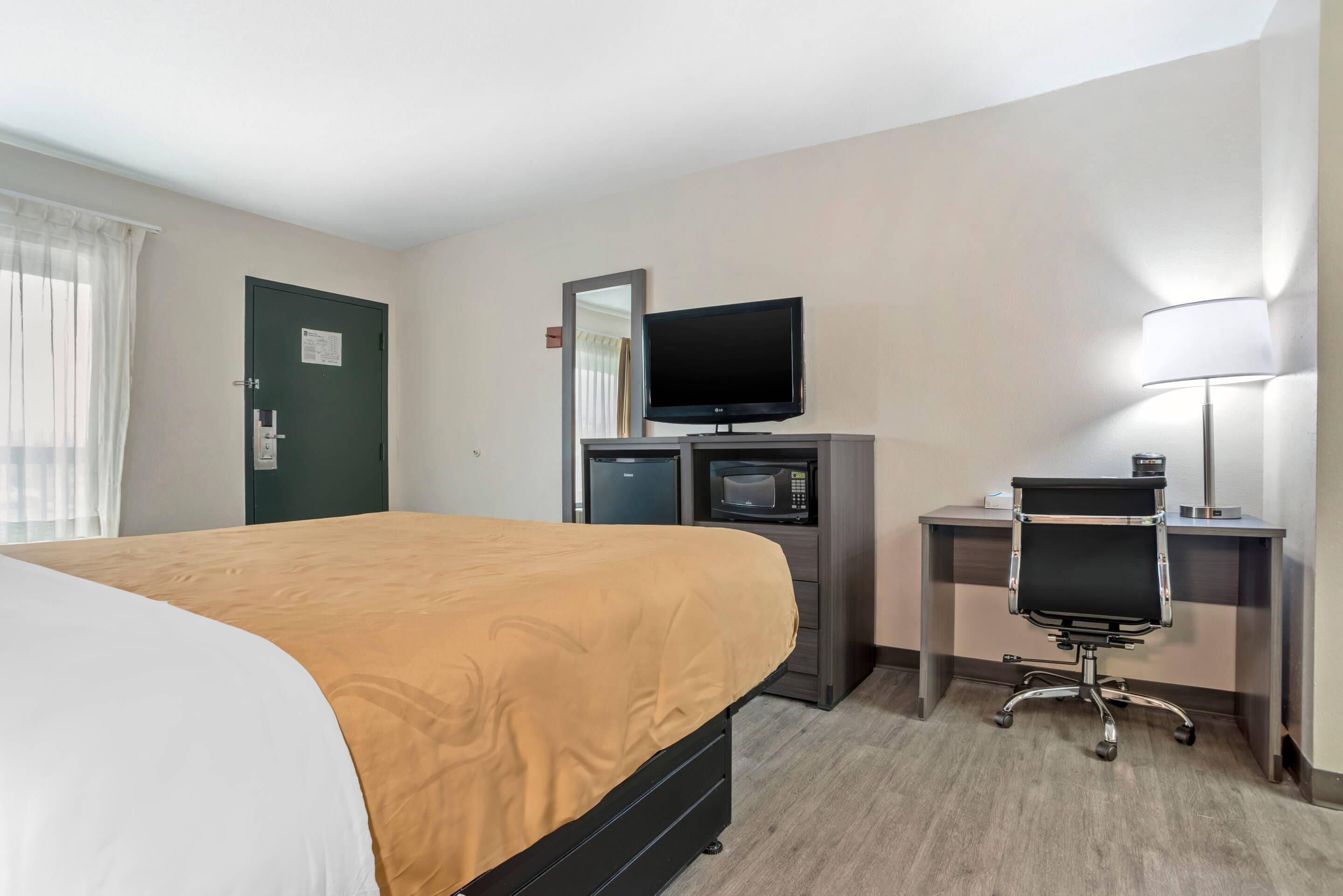 A hotel room with a bed, a desk with a computer, a television, and a microwave.