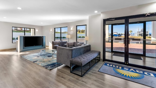 A modern hotel lobby with a large seating area, a flat-screen TV, and large windows offering views of the outdoors. - Days Inn by Wyndham Enterprise (Enterprise)