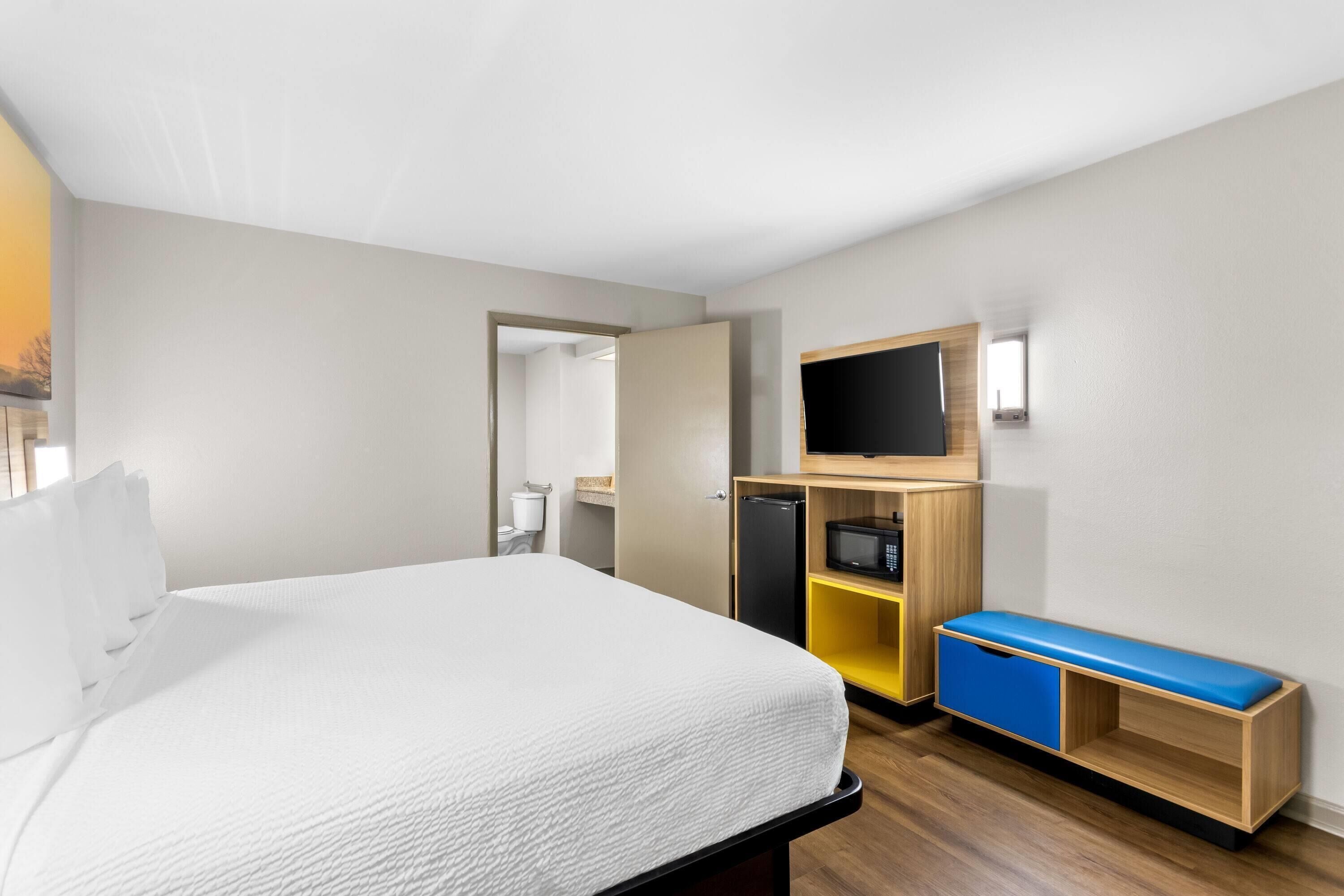 A hotel room with a bed, a TV, a desk with drawers, and a small kitchenette.