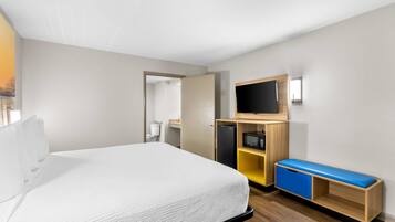 A hotel room with a bed, a TV, a desk with drawers, and a small kitchenette.