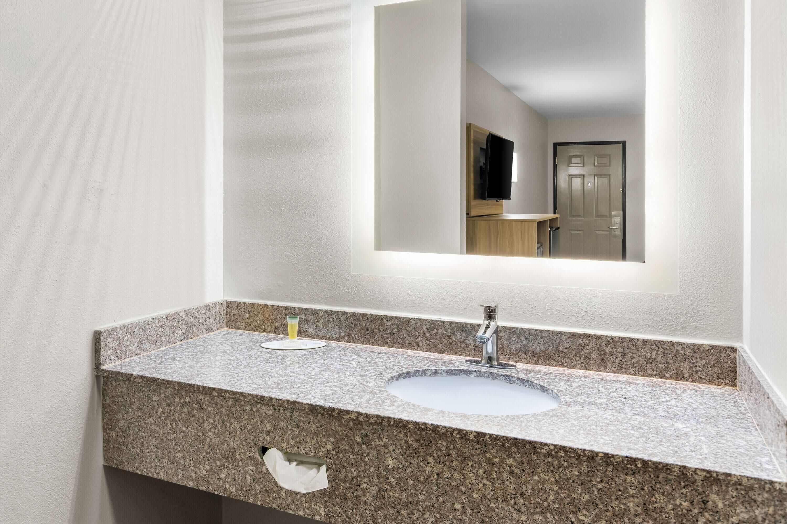 A bathroom with a granite countertop, a sink, a mirror, and a towel dispenser.