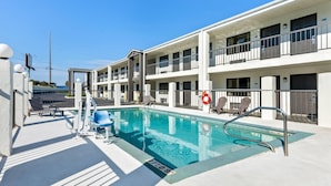 A swimming pool with lounge chairs and a lifeguard chair, surrounded by a multi-story building with balconies. - Days Inn by Wyndham Enterprise (Enterprise)