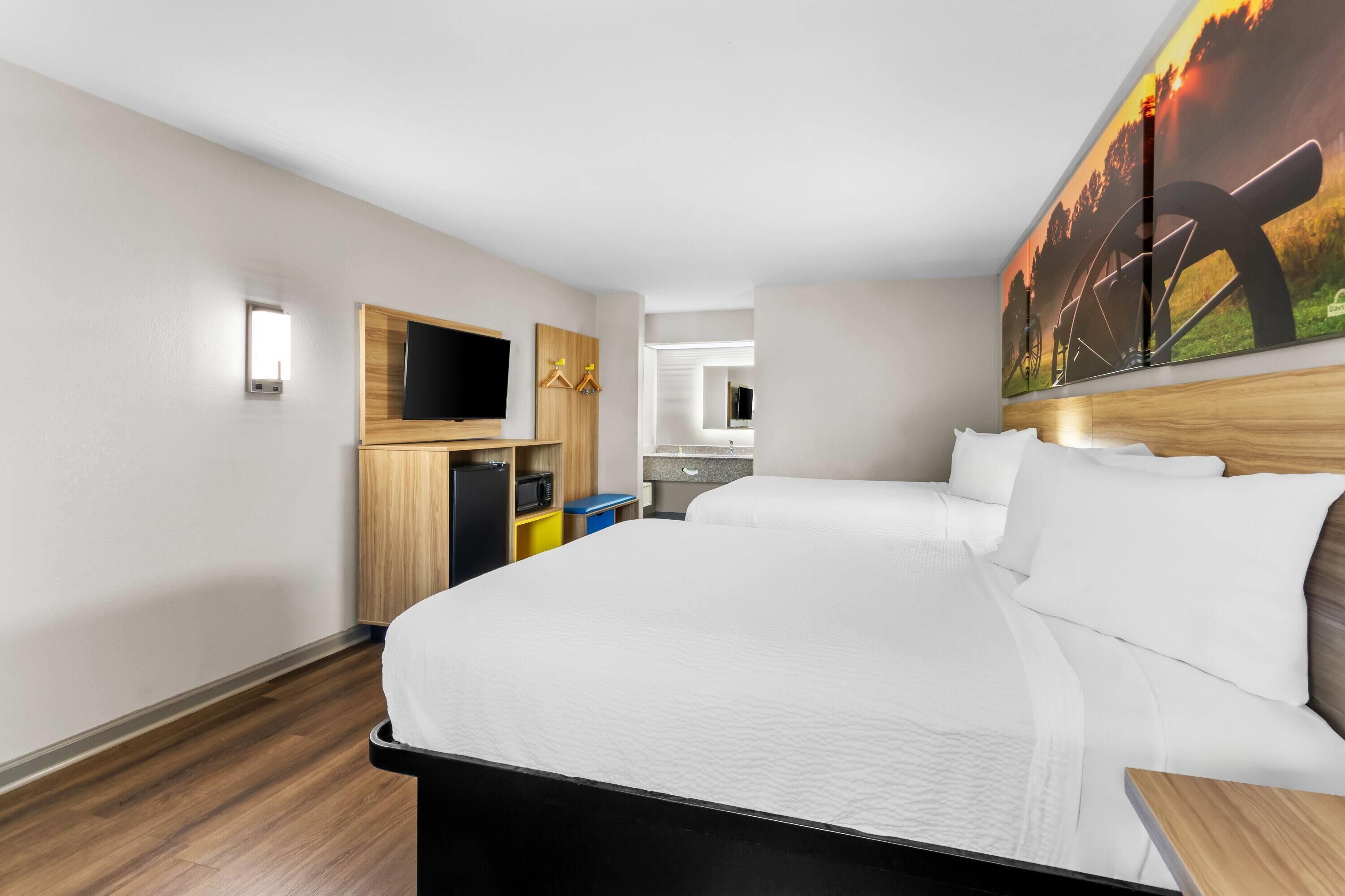 Una habitación de hotel con una cama grande, un televisor, un armario de madera y un cuadro en la pared.