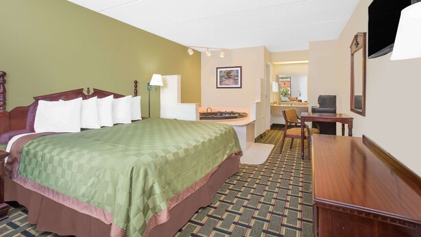 A hotel room with a large bed, a desk, a chair, a small table, a mirror, and a television. - Days Inn by Wyndham Eufaula AL (Eufaula)