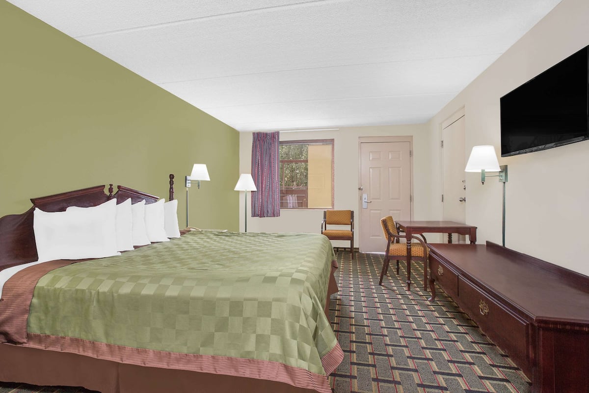 Quarto de hotel com cama, escrivaninha, cadeira, televisão e janela com cortinas.