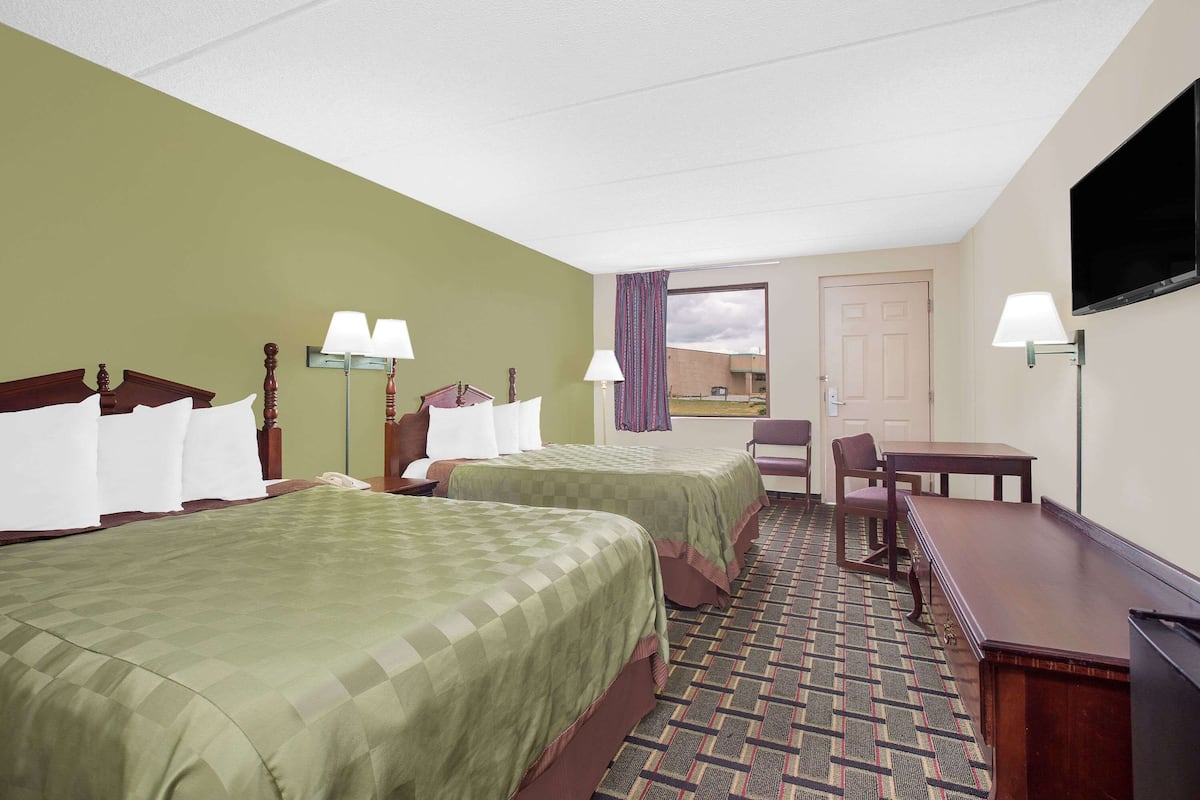 Quarto de hotel com duas camas, uma escrivaninha, uma cadeira, uma televisão e uma janela com cortinas.