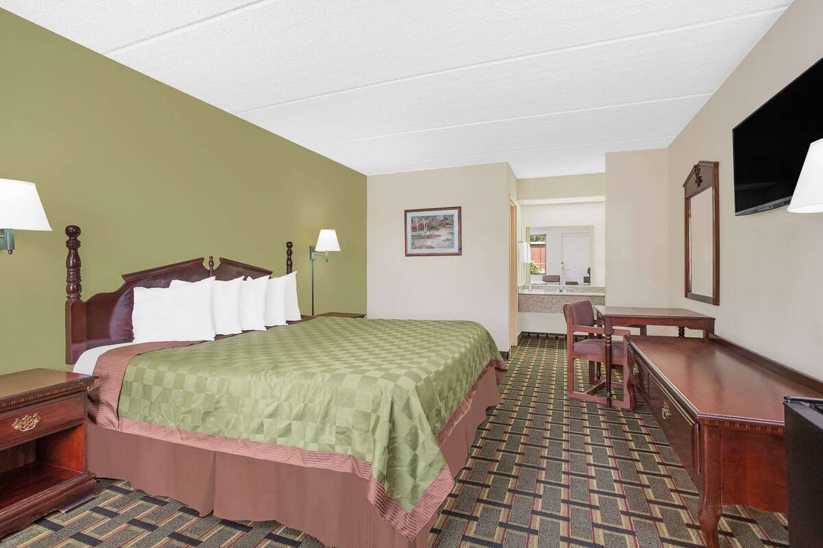 Quarto de hotel com cama, escrivaninha, cadeira e televisão.