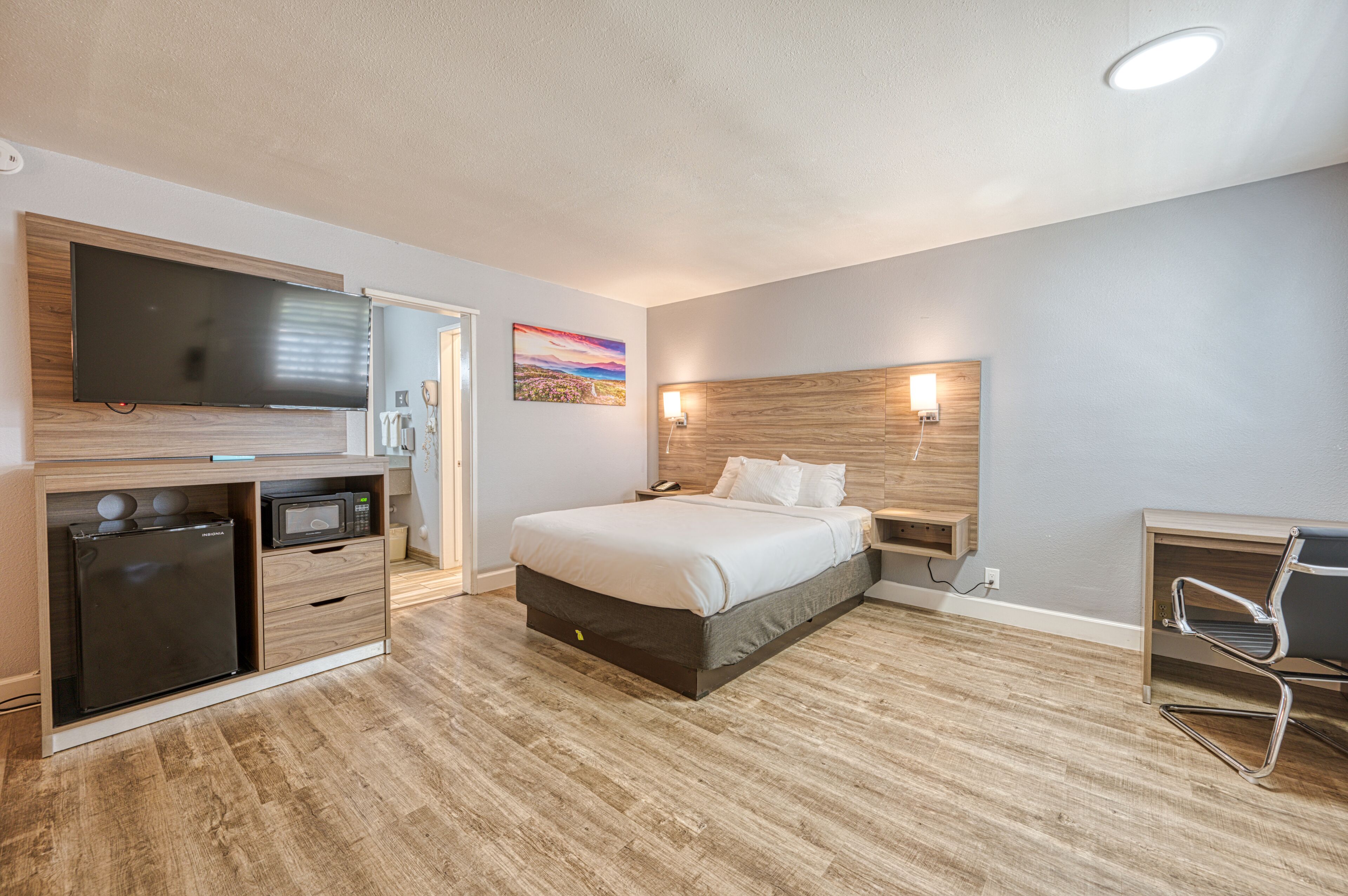 A modern hotel room with a bed, a flat-screen TV, a microwave, and a desk with a chair.