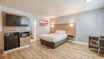 A modern hotel room with a bed, a flat-screen TV, a microwave, and a desk with a chair.