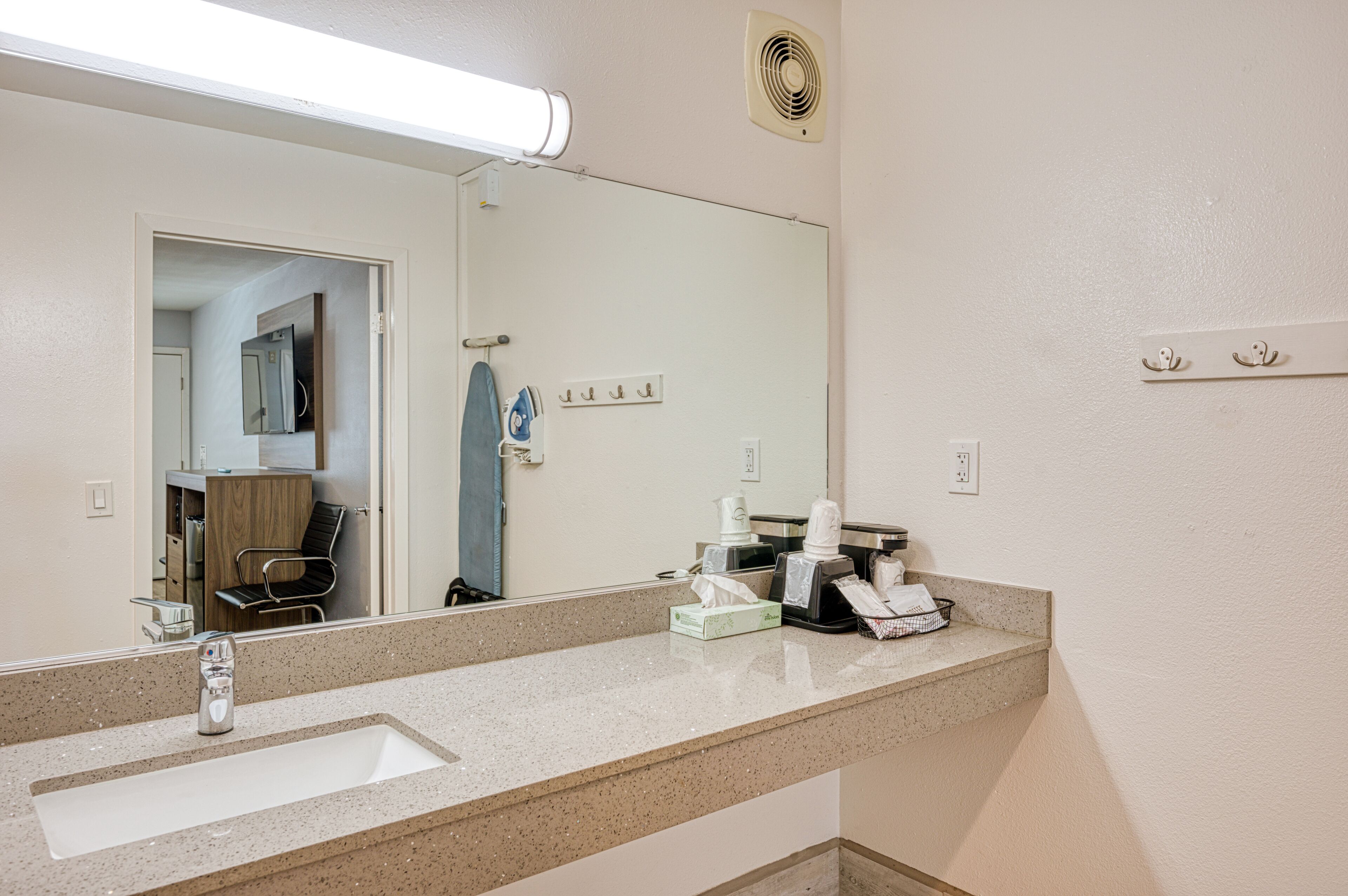 Casa de banho de hotel com um espelho grande, uma pia, um porta-toalhas e um ventilador.
