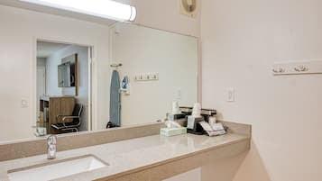 Casa de banho de hotel com um espelho grande, uma pia, um porta-toalhas e um ventilador.