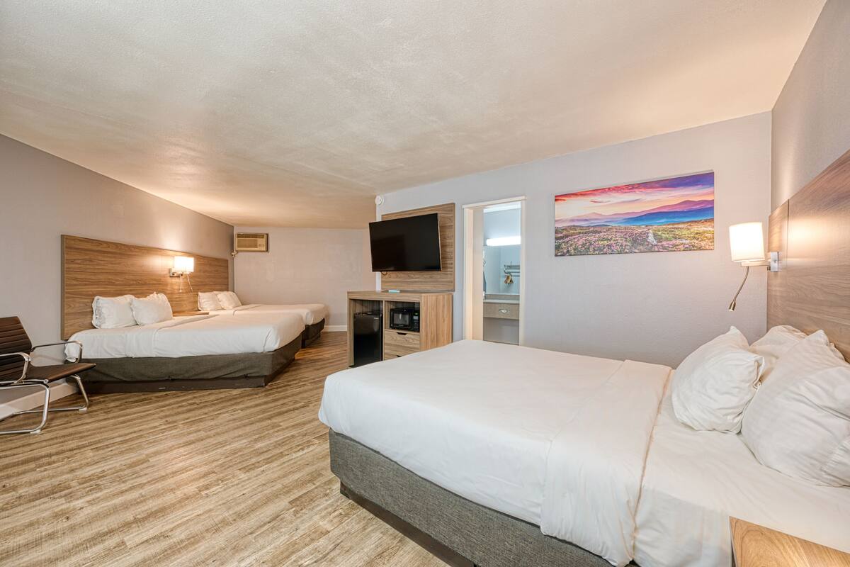 Une chambre d’hôtel avec deux lits, un bureau, une télévision et un tableau au mur.