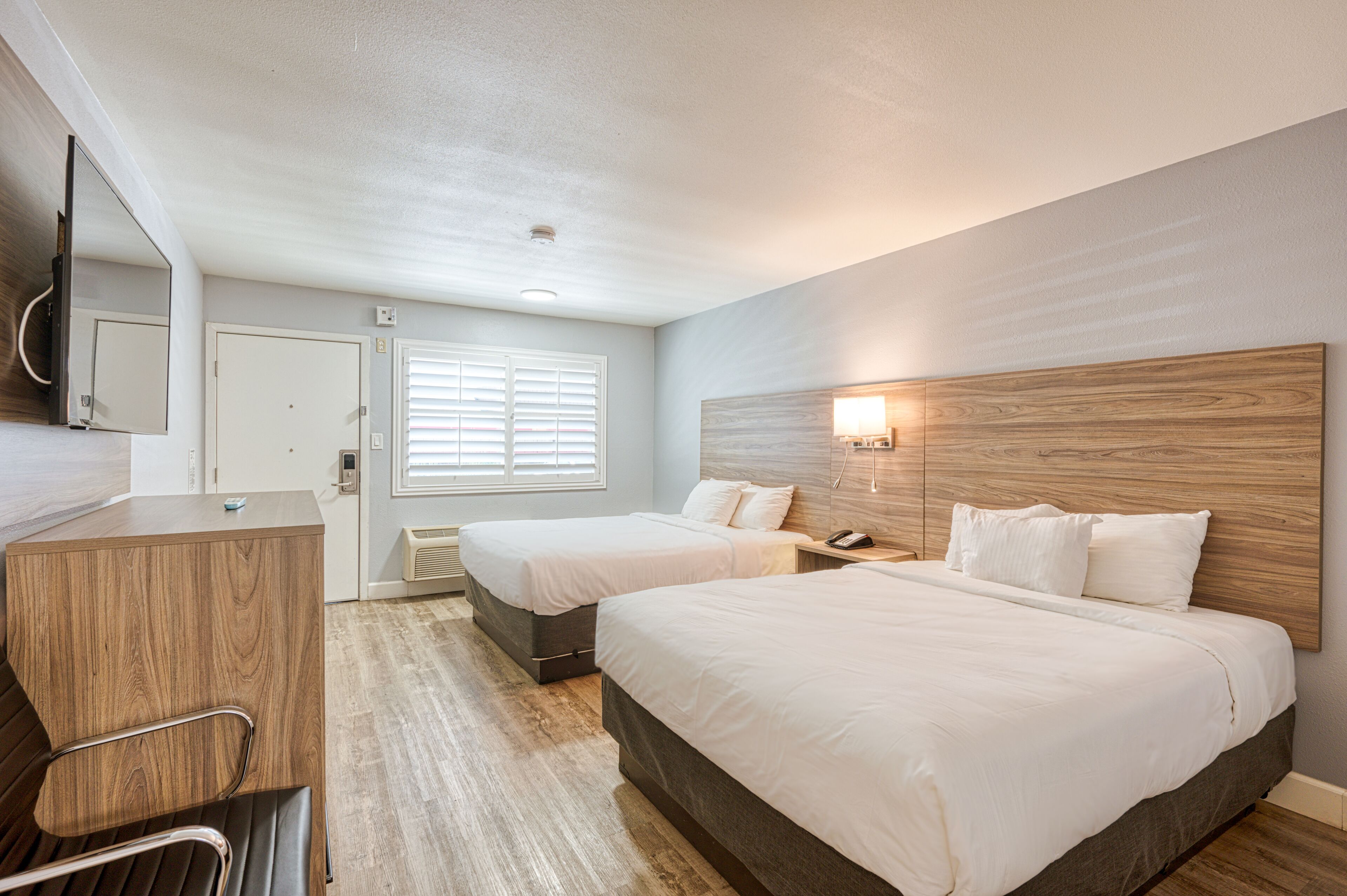 Habitación de hotel con dos camas, un escritorio, una silla, un espejo y una lámpara fijada a la pared.
