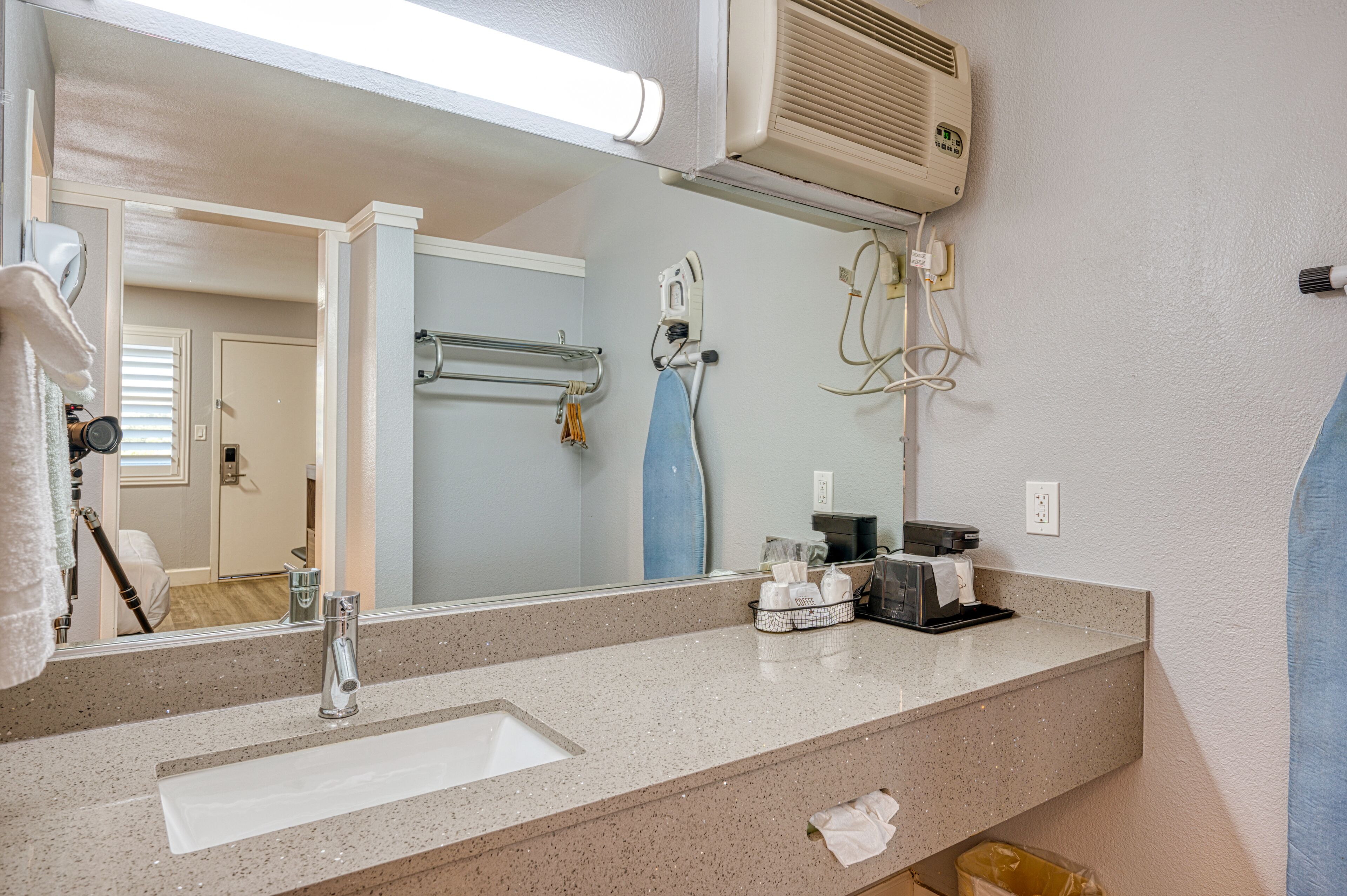 A bathroom with a large mirror, a sink, a towel rack, a hairdryer, and a towel hanging on the wall.