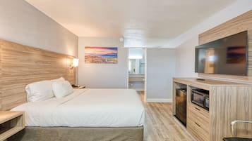 A modern hotel room with a large bed, a TV, a microwave, and a wooden headboard.