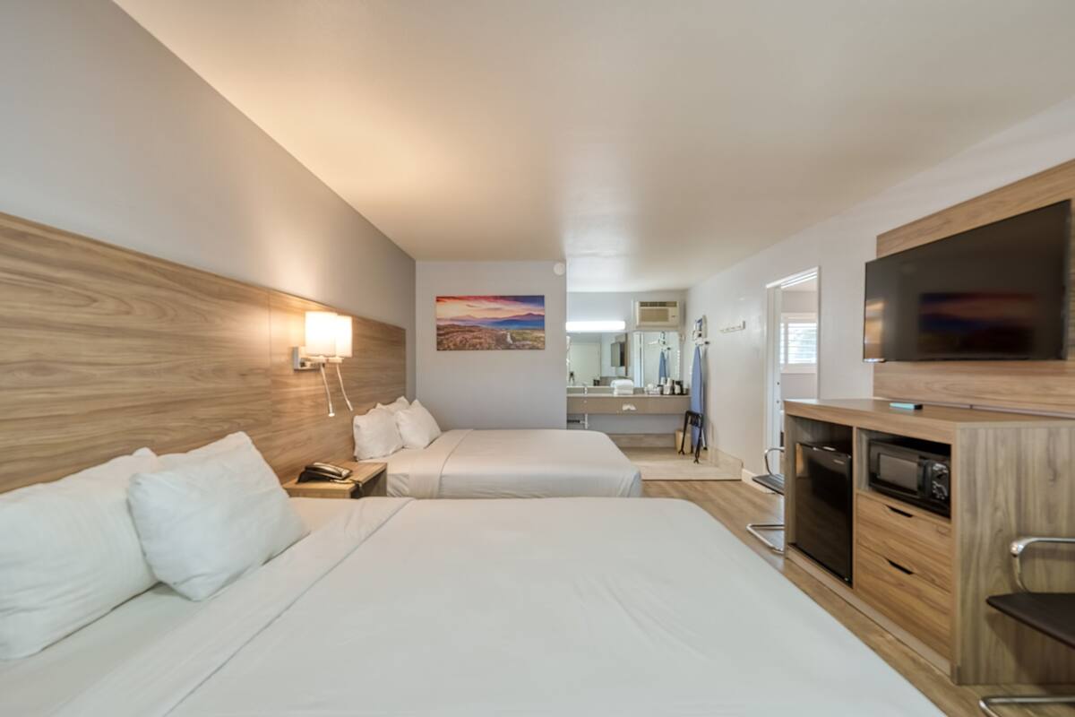 Une chambre d’hôtel avec deux lits, une tête de lit en bois, une télévision, un four à micro-ondes et une petite kitchenette.