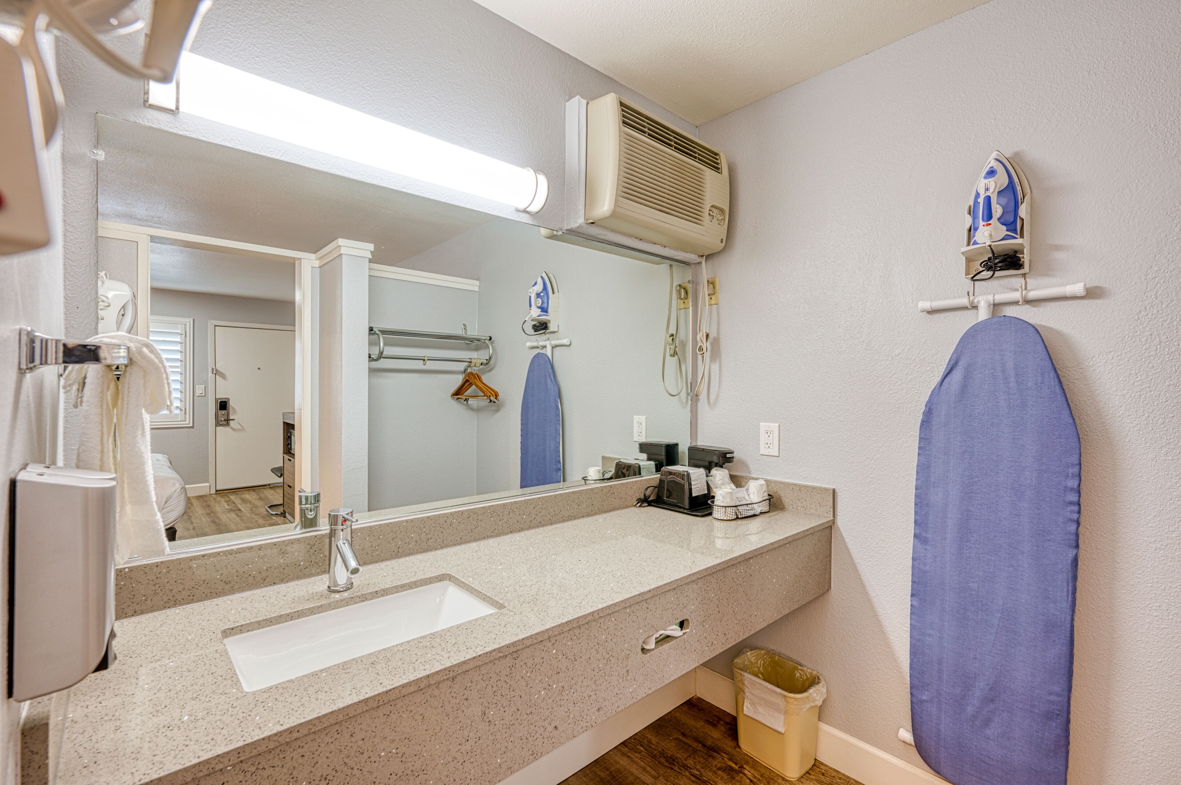 A bathroom with a sink, mirror, towel rack, and an ironing board.