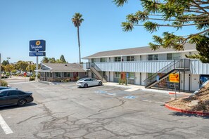 Un estacionamiento con el letrero VAGABOND INN, un edificio con una escalera y una palmera.