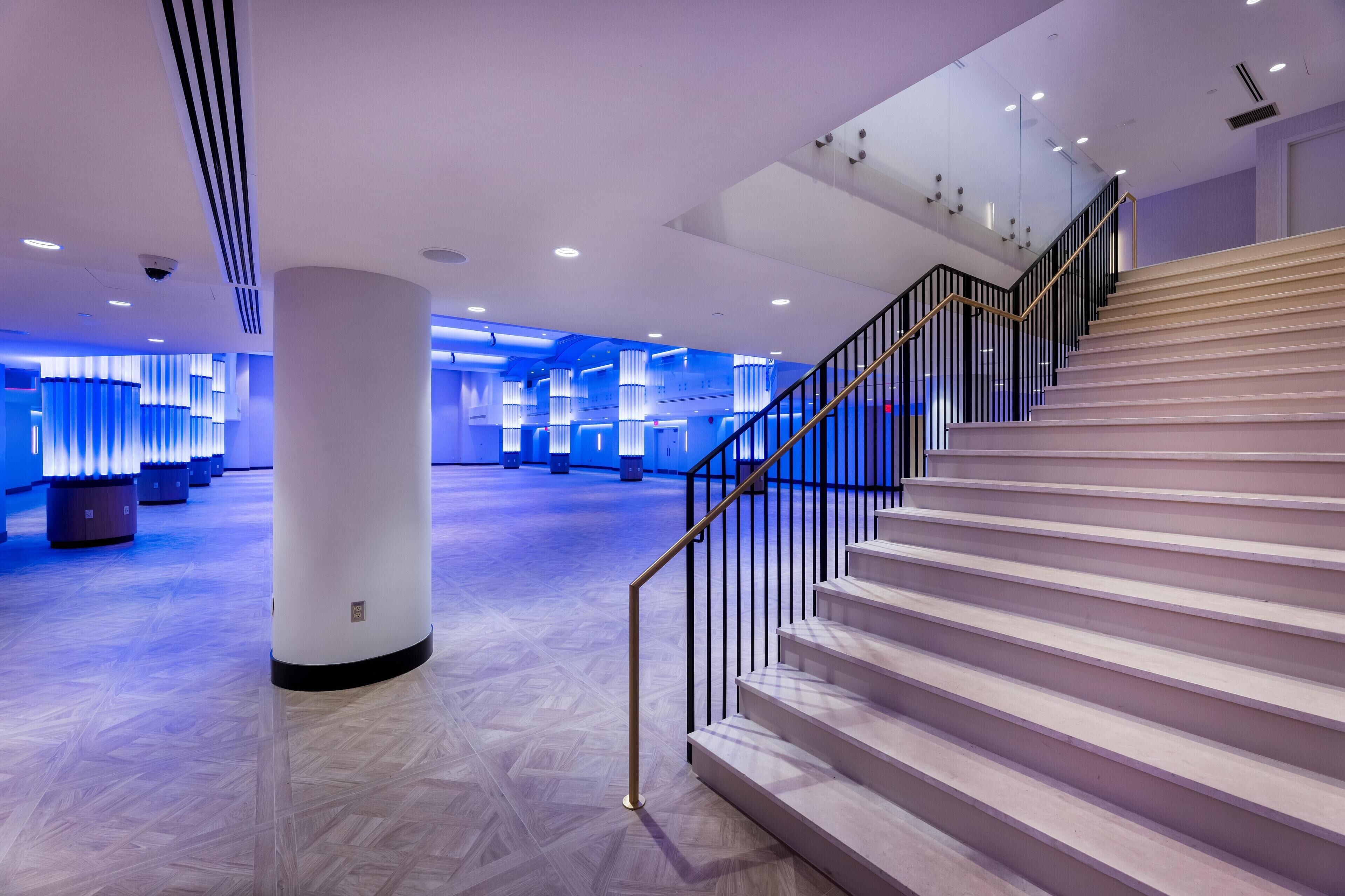 A modern hotel lobby with a grand staircase, polished wooden floors, and ambient lighting.