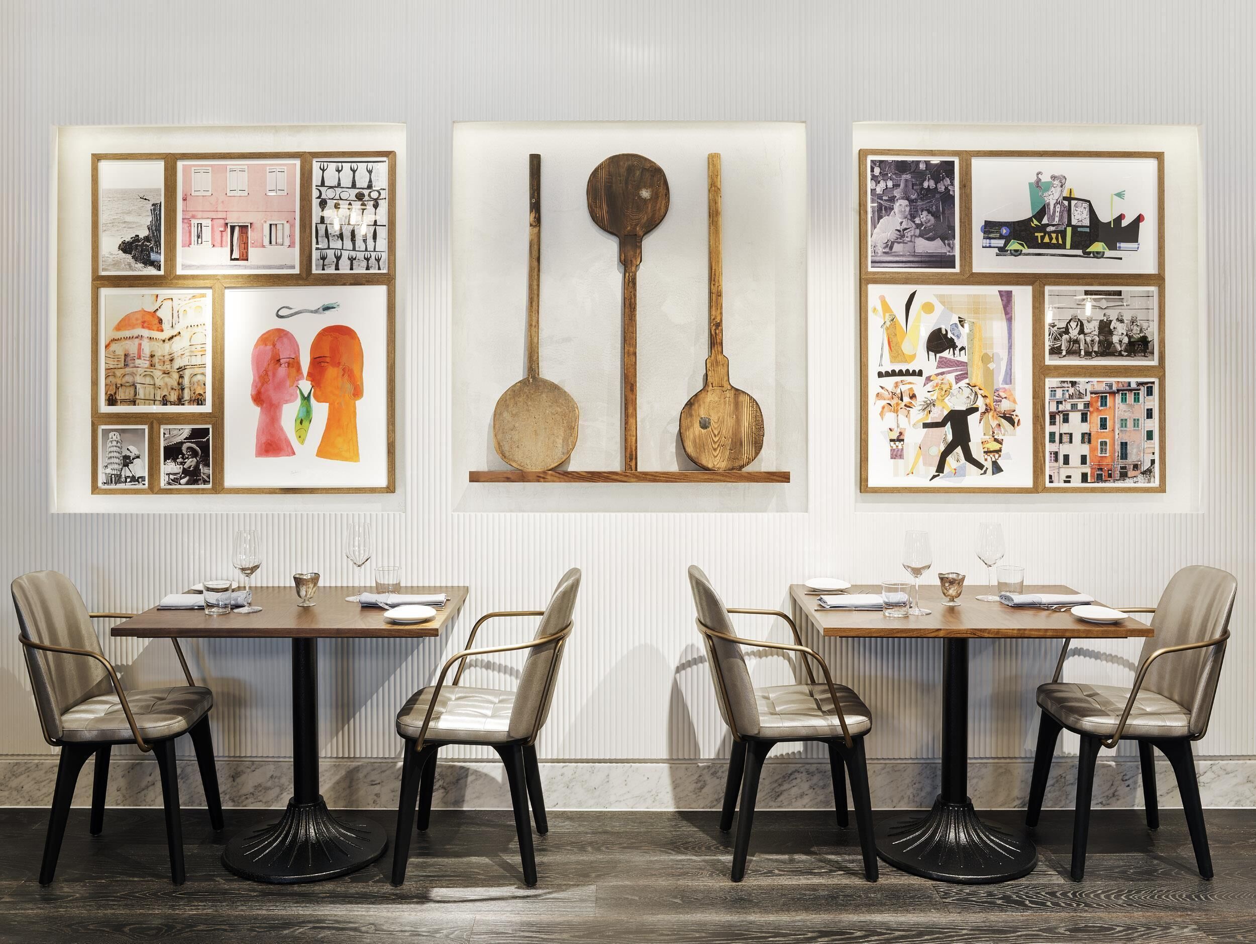 A dining area with two tables, each with a chair, and a wall decorated with framed artwork.