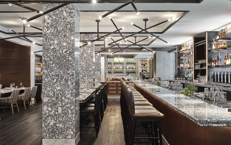 A modern bar area with a marble column, wooden bar stools, and a long counter.