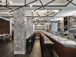 A modern bar area with a marble column, wooden bar stools, and a long counter. - Hamilton Hotel Washington DC (Washington)