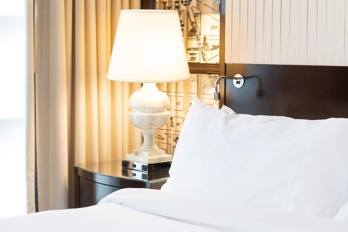 A neatly made bed with white linens, a bedside lamp, and a wall with a geometric pattern.