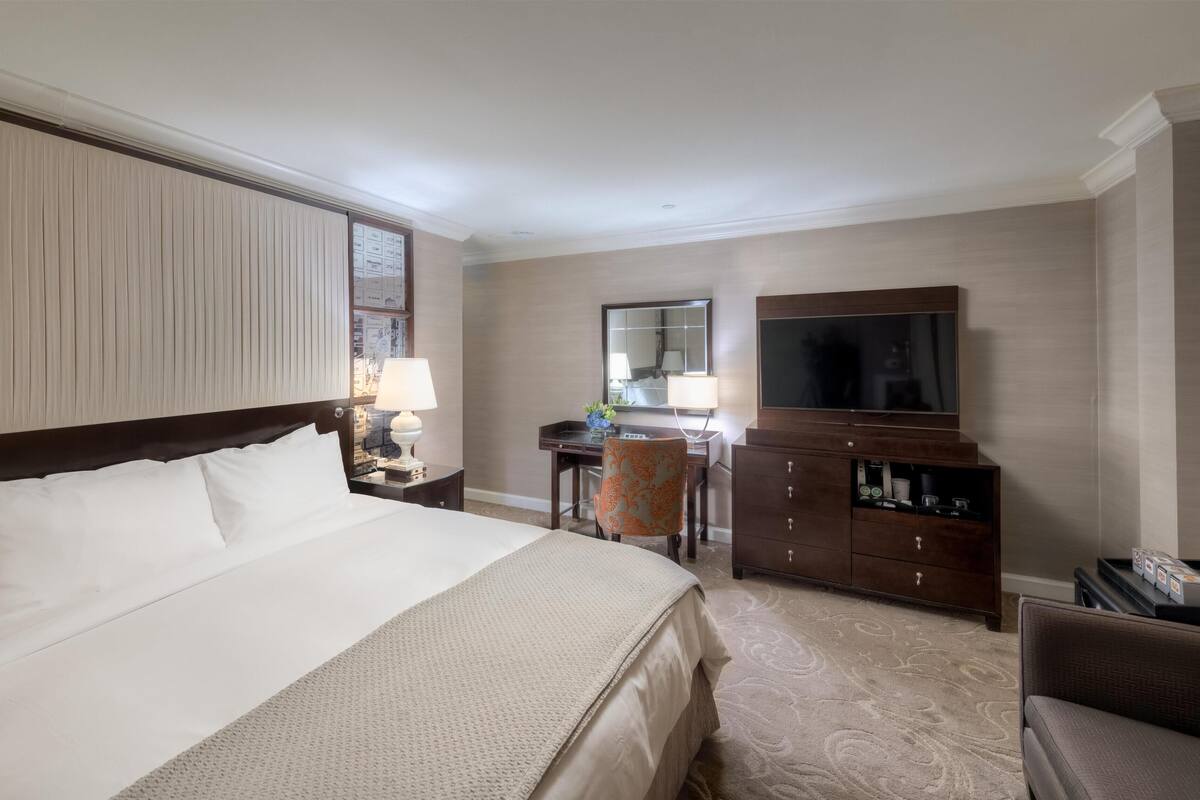 A hotel room with a large bed, a desk with a chair, a television, and a wardrobe.