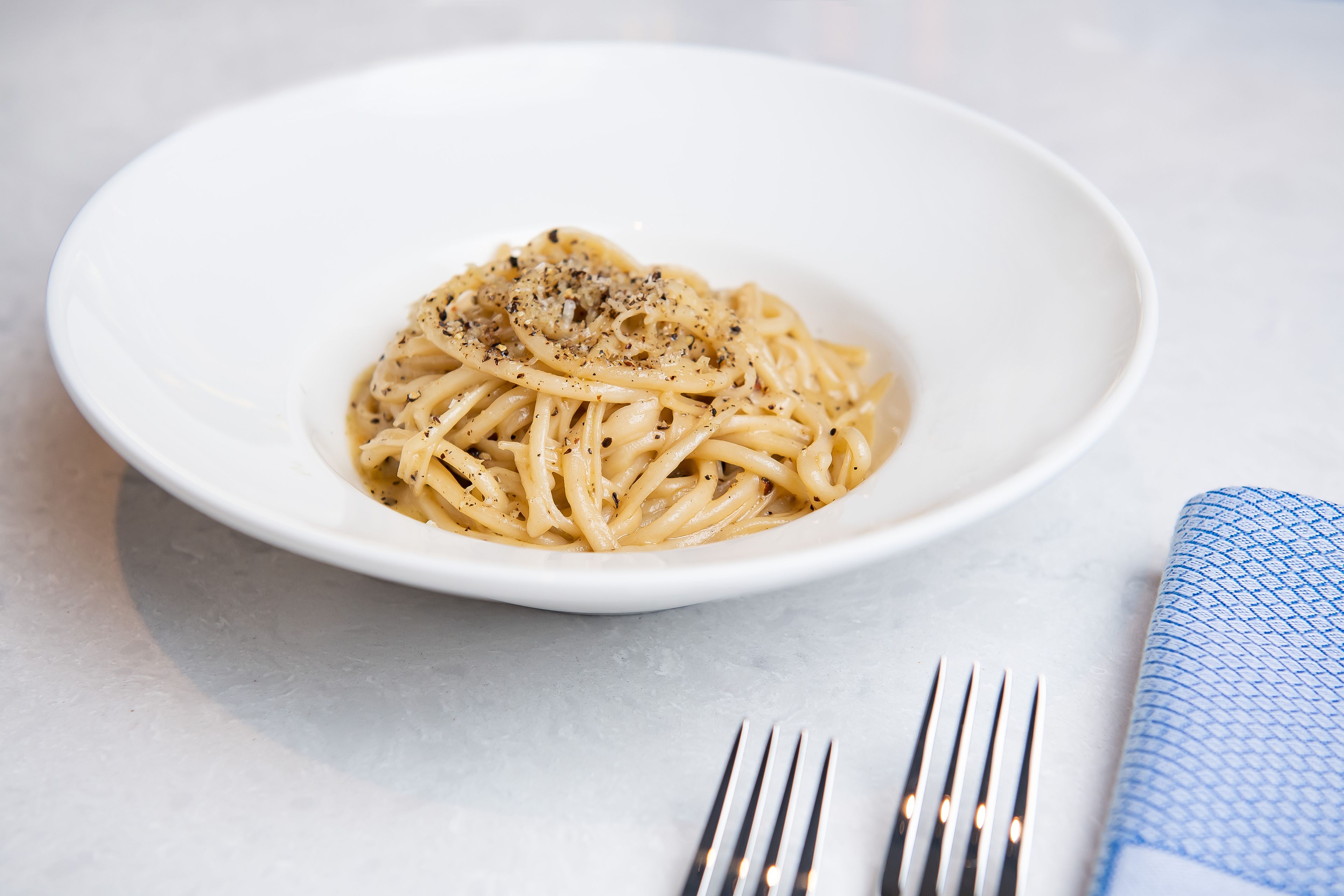 A bowl of spaghetti with a sprinkle of black pepper on a white plate.