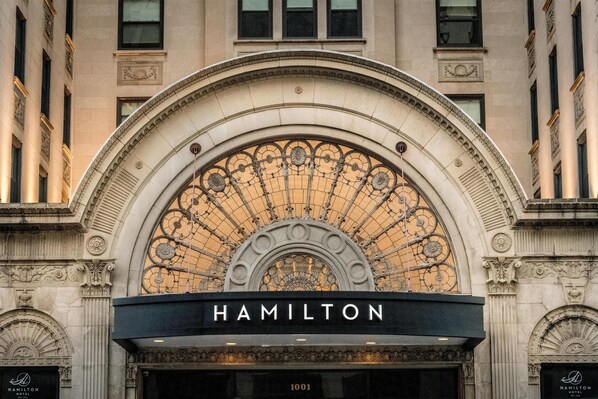 The exterior of the Hamilton Hotel with a prominent arched entrance and a large, ornate window above the entrance.
