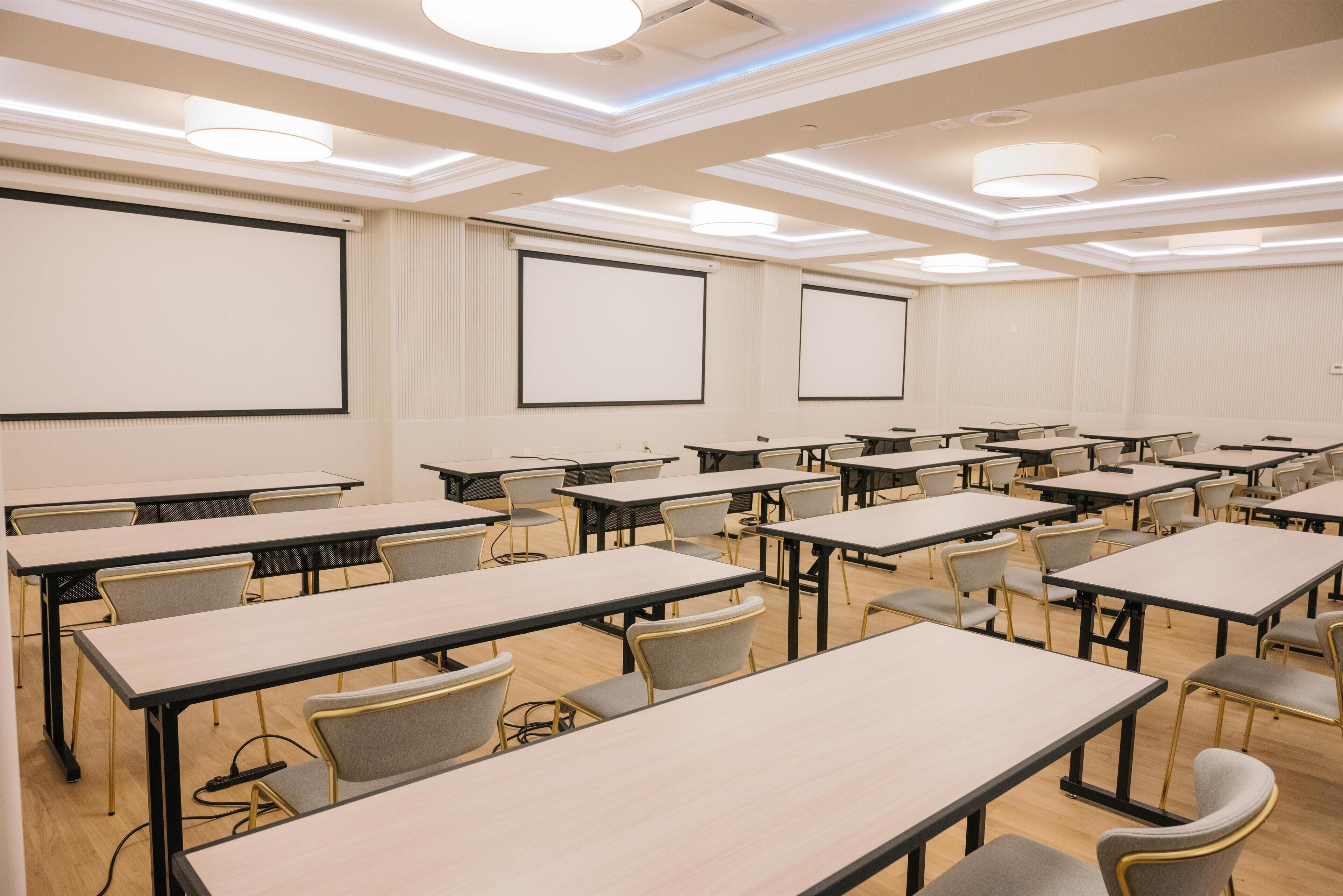 A conference room with multiple tables and chairs, large projection screens, and ceiling lights.