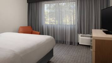 A hotel room with a bed, an orange chair, a television, and a window with curtains.