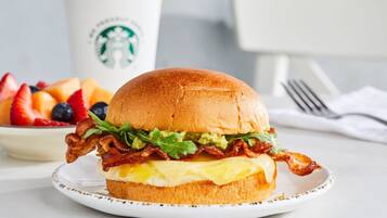 A breakfast sandwich on a plate with a Starbucks cup in the background.