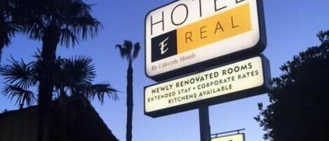 Señal de hotel con el nombre "Hotel Real" que anuncia habitaciones renovadas, tarifas para estancias prolongadas y cocinas disponibles.