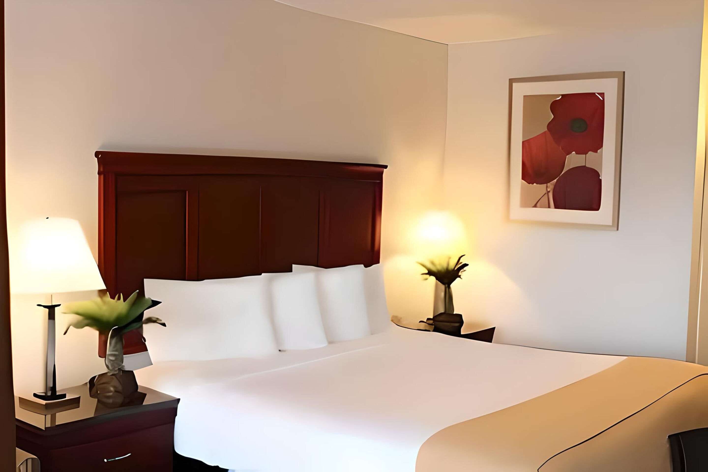A hotel room with a large bed, two bedside tables, a nightstand, and a framed artwork on the wall.