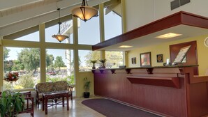 A reception area with a wooden reception desk, a sofa, and chairs. There are large windows providing a view of the outdoors. - Rodeway Inn Santa Clara El Camino Real (Santa Clara)