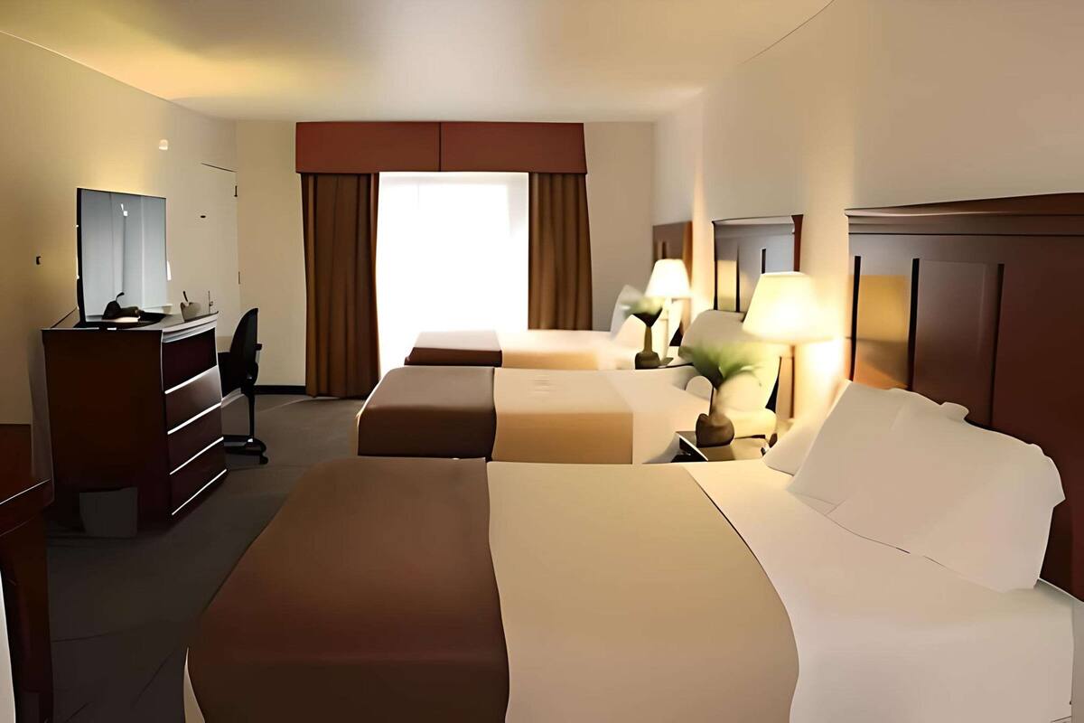 A hotel room with a large bed, a smaller bed, a desk with a chair, a mirror, and a window with curtains.